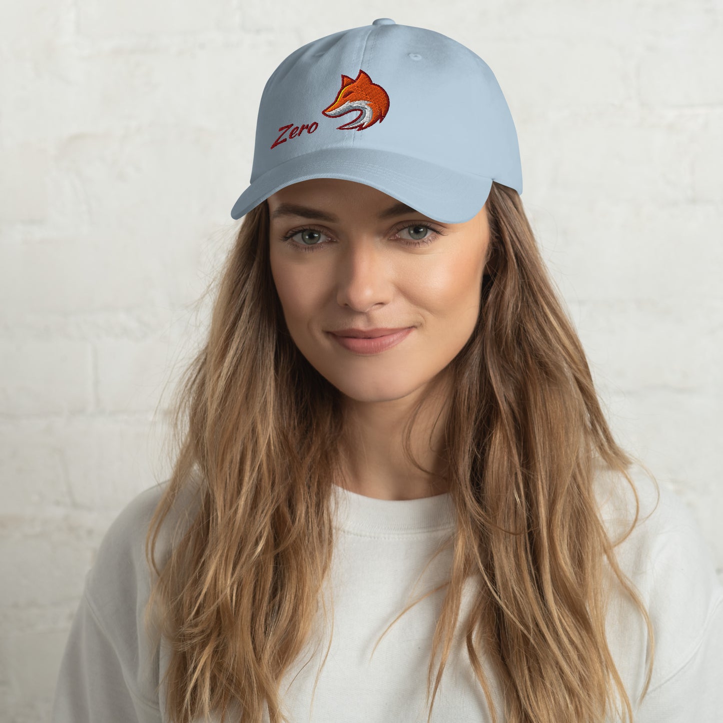 Woman wearing light blue baseball cap with embroidered fox and the word "Zero" on the front, suggesting the phrase "Zero Fox" or "Zero Fcks."